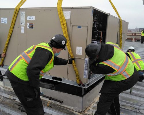 Four Men Installing New HVAC Unit On Rooftop